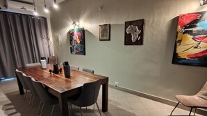Een eetgedeelte met een houten tafel, stoelen en kunstwerken aan de wanden.