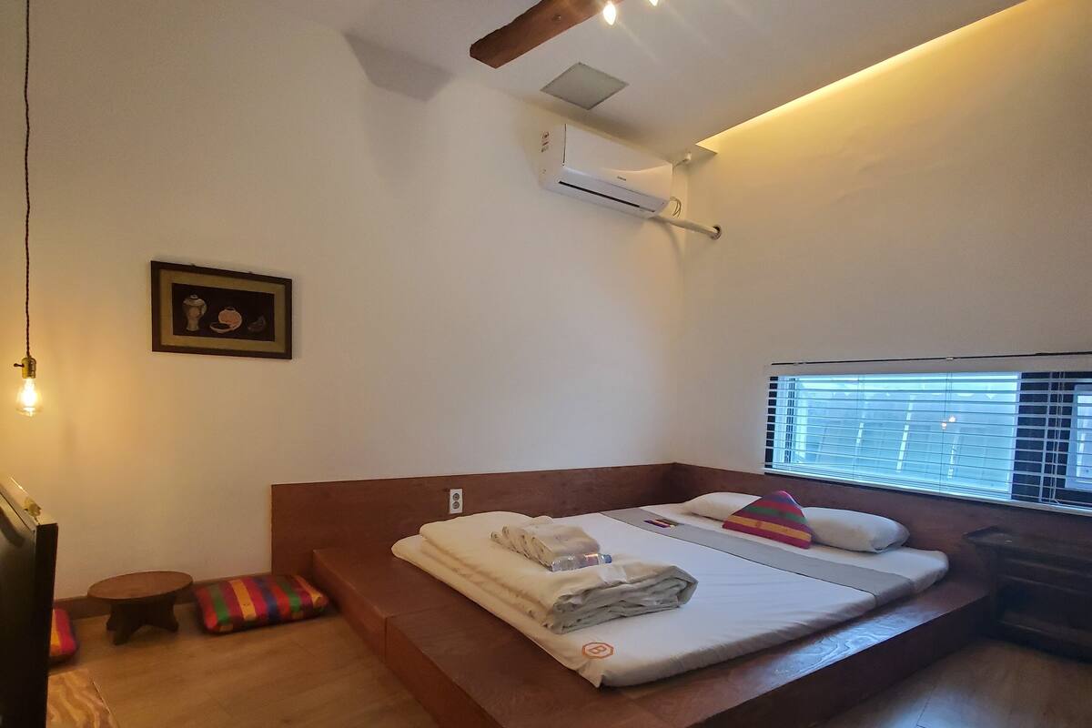 A modern bedroom with a wooden platform bed, a small round table, and a colorful striped cushion.
