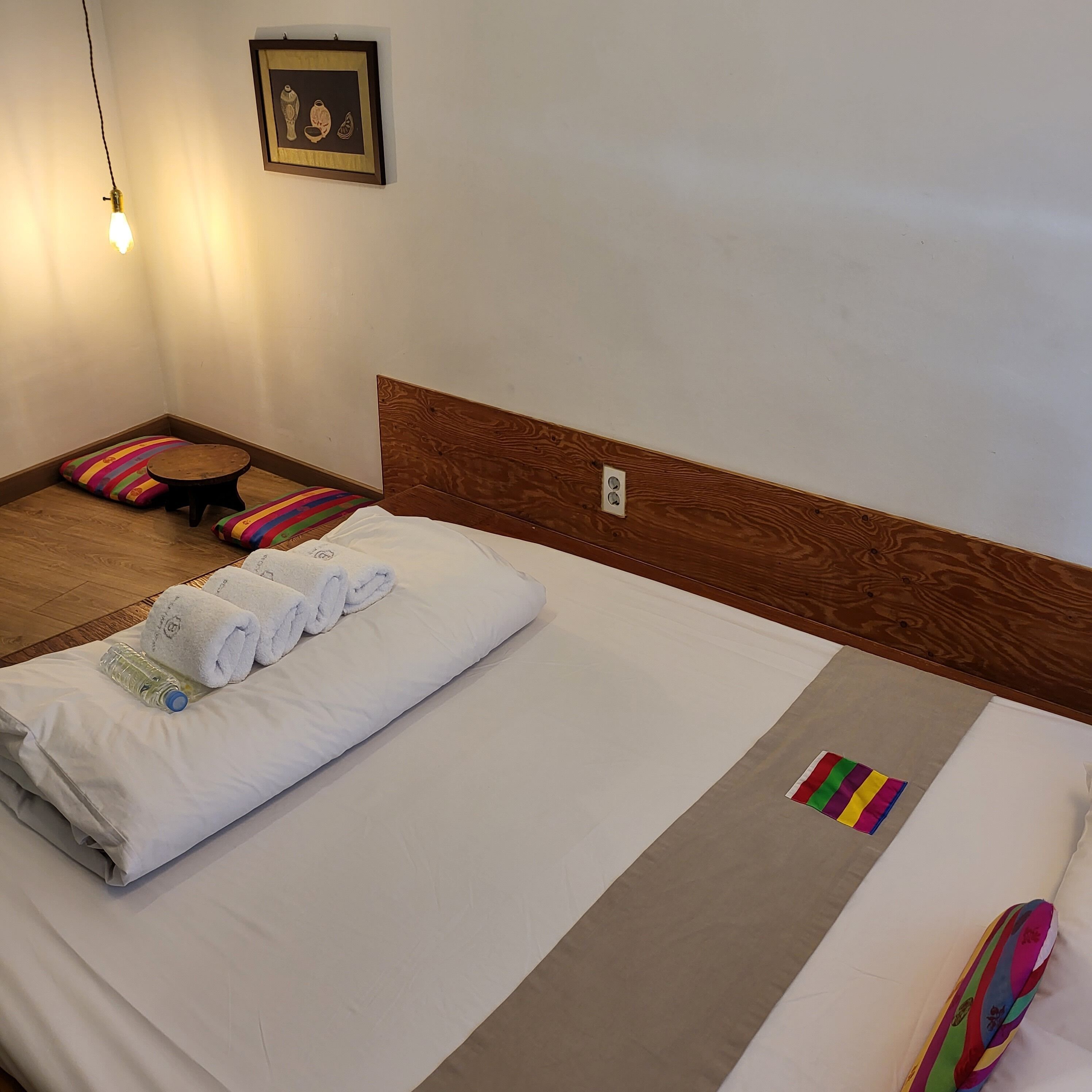 Una cama bien hecha con sábanas blancas, un cabecero de madera y un colorido tapete a rayas en el suelo.