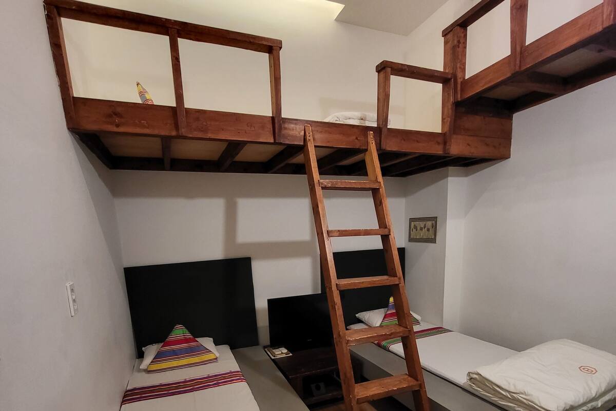 A dormitory room with bunk beds, a wooden ladder, and a small desk.