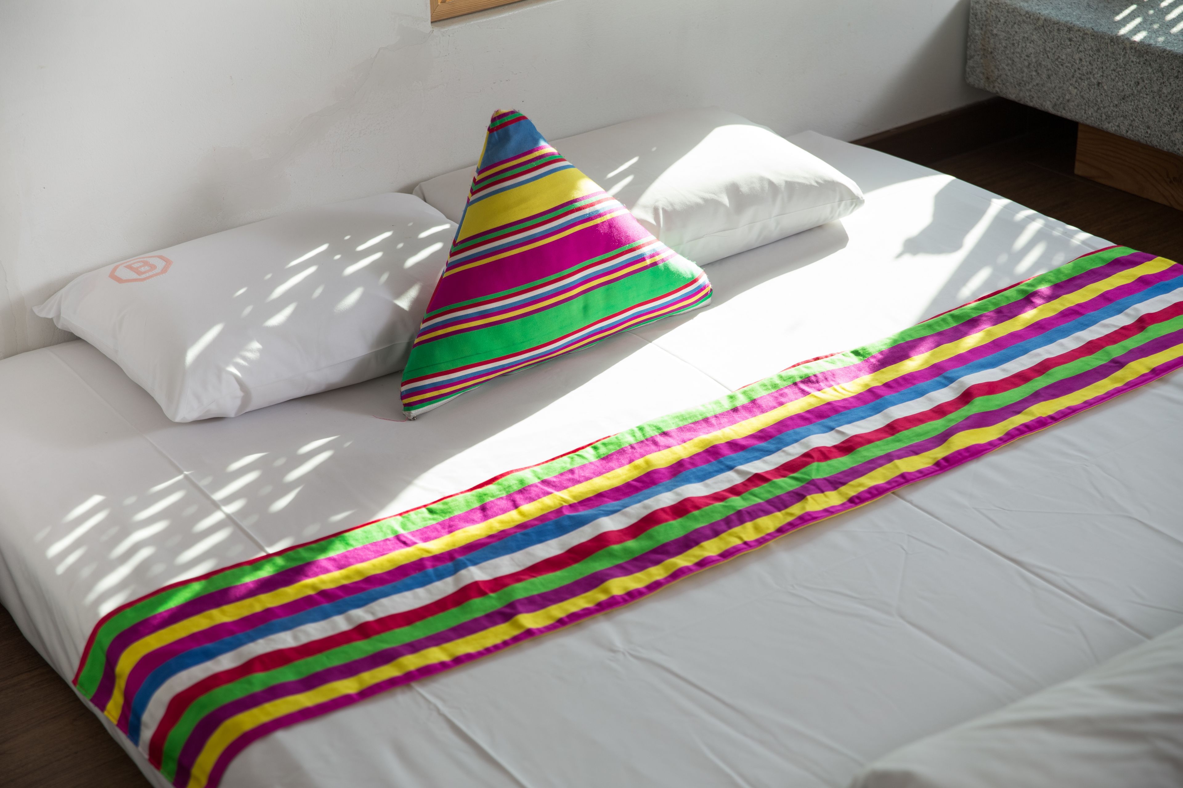 A bed with white bedding, a colorful striped blanket, and a multicolored pillow.