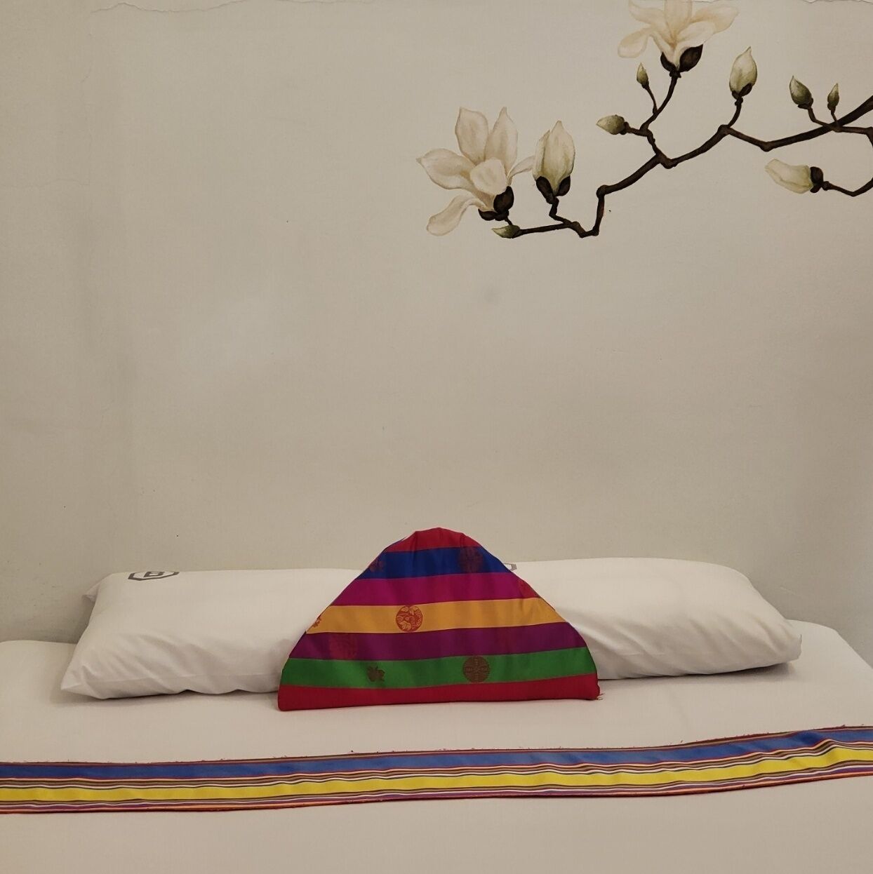 Una cama con almohadas blancas y una almohada con rayas de arcoíris de colores.