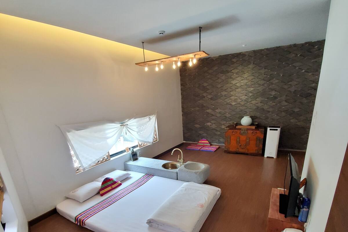 A modern bedroom with a large bed, a bedside table, a small cabinet, and a stone wall.
