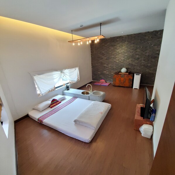 A modern bedroom with a large bed, a bedside table, a small cabinet, and a stone wall. - Becky Guesthouse (Jeonju)