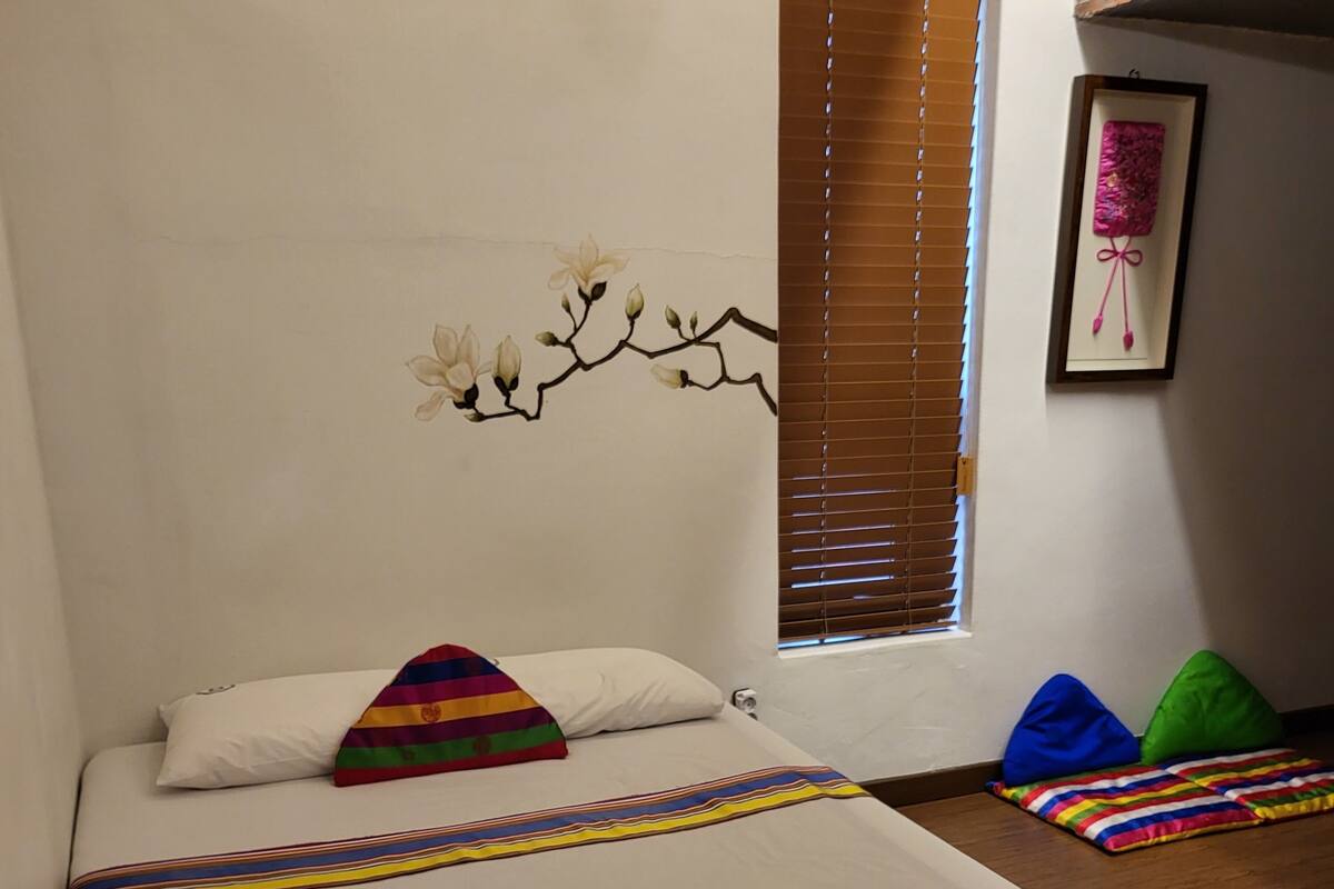 A neatly made bed with white linens, a colorful striped blanket, and rolled towels on a white pillow.