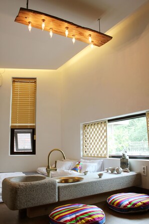 A modern bathroom with a stone sink, a wooden light fixture, a window with blinds, and a colorful cushion. - Becky Guesthouse (Jeonju)