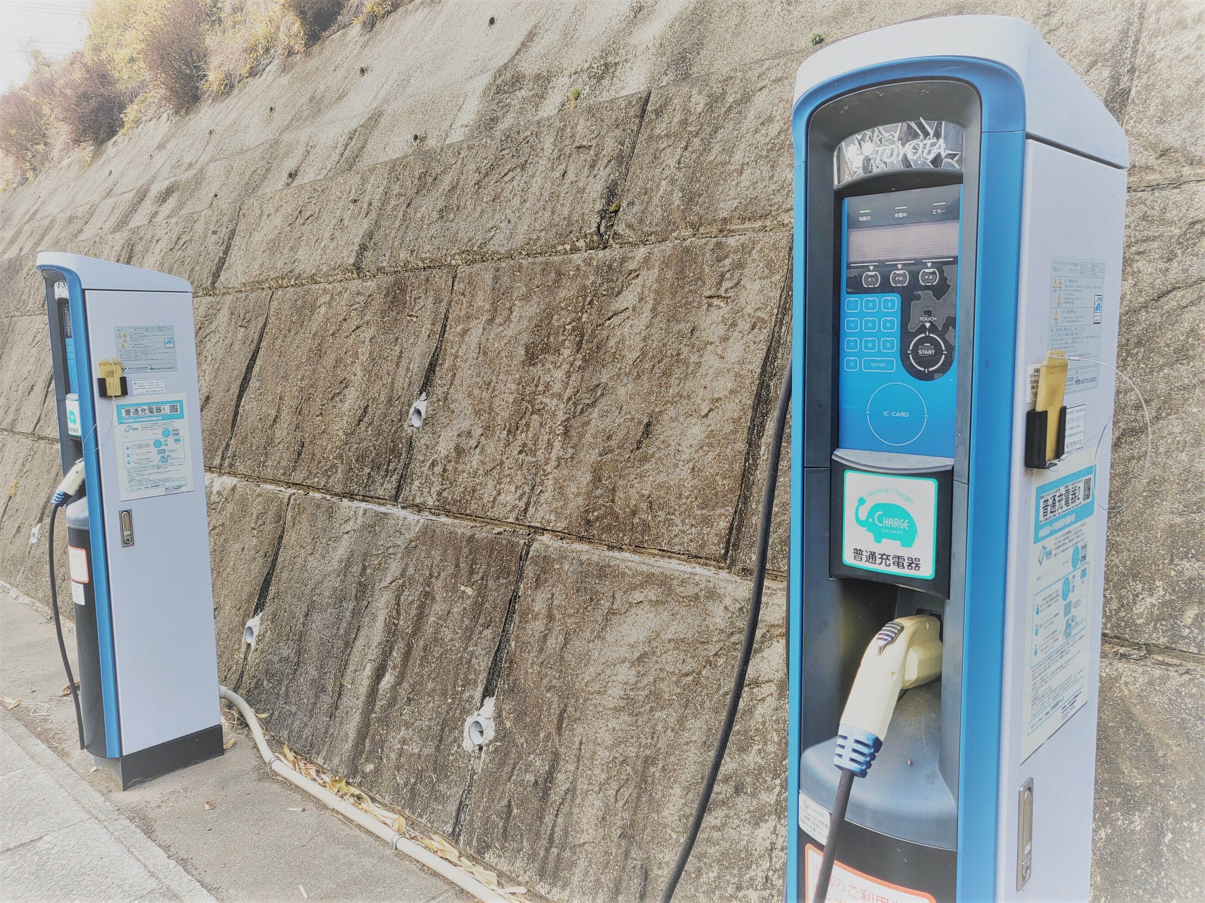 Dos estaciones de carga para vehículos eléctricos, con indicaciones y un cable conectado a una de ellas.