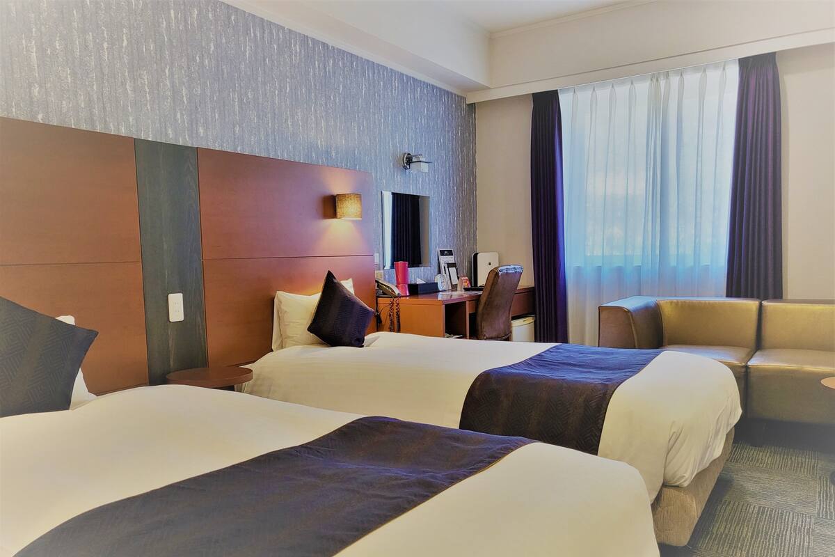Ein Hotelzimmer mit zwei Betten, einem Schreibtisch, einem Sessel und einer Couch.
