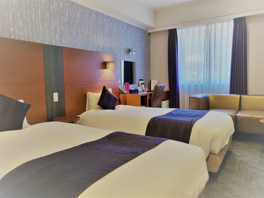 Une chambre d’hôtel avec deux lits, un bureau, une chaise et un canapé.