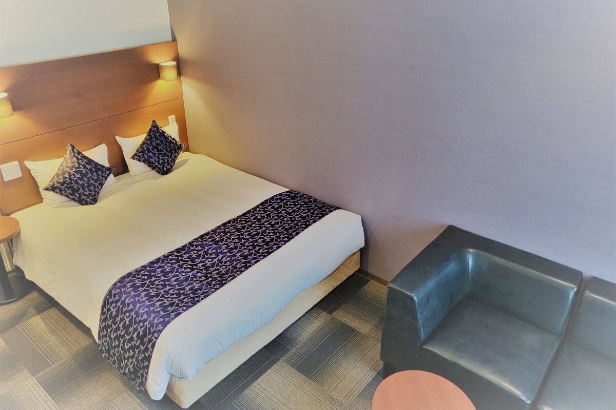 Ein Hotelzimmer mit einem ordentlich bezogenen Bett, einem Nachttisch und einem kleinen runden Tisch.