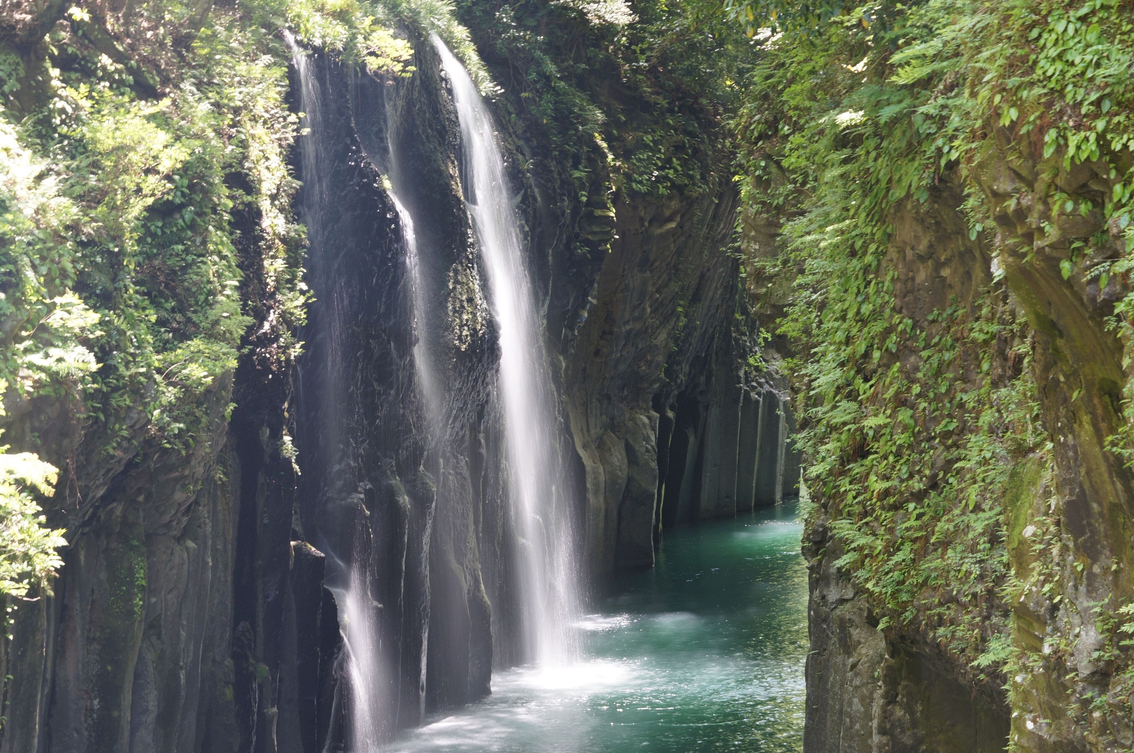 A waterfall cascading down a rocky cliff surrounded by lush greenery.