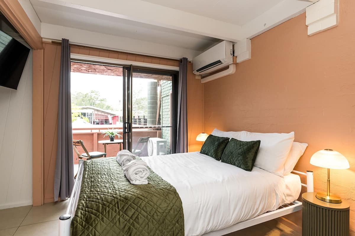 A hotel room with a bed, a bedside lamp, a TV, and a sliding glass door leading to an outdoor area.