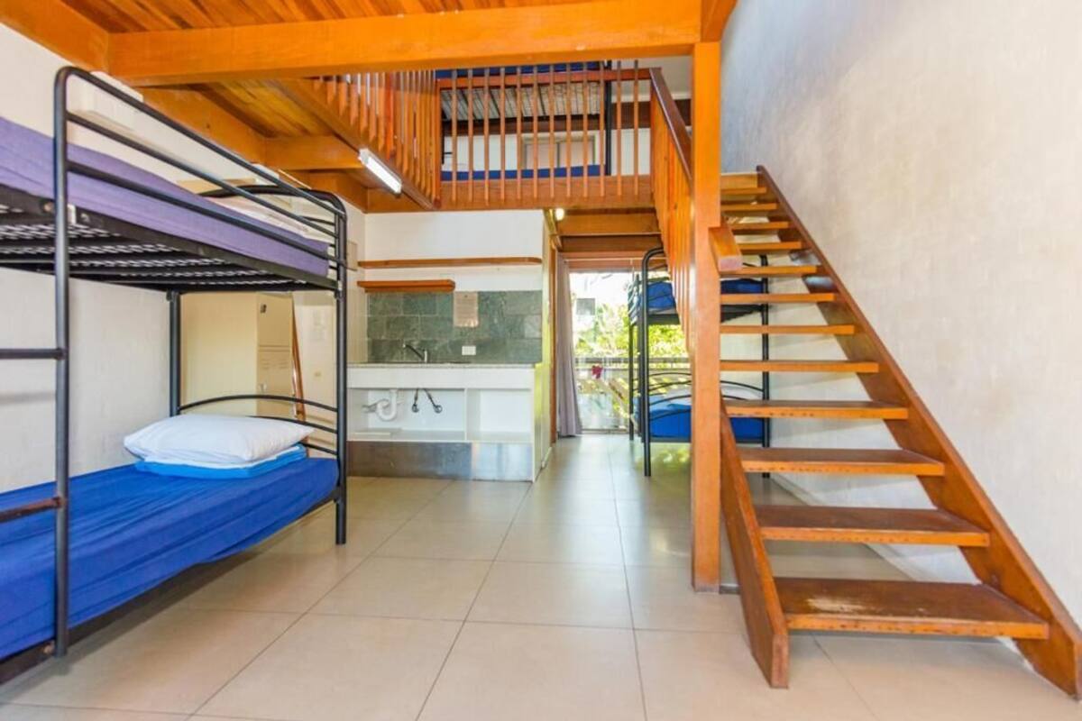 Un dormitorio con literas, una escalera de madera y un lavabo.
