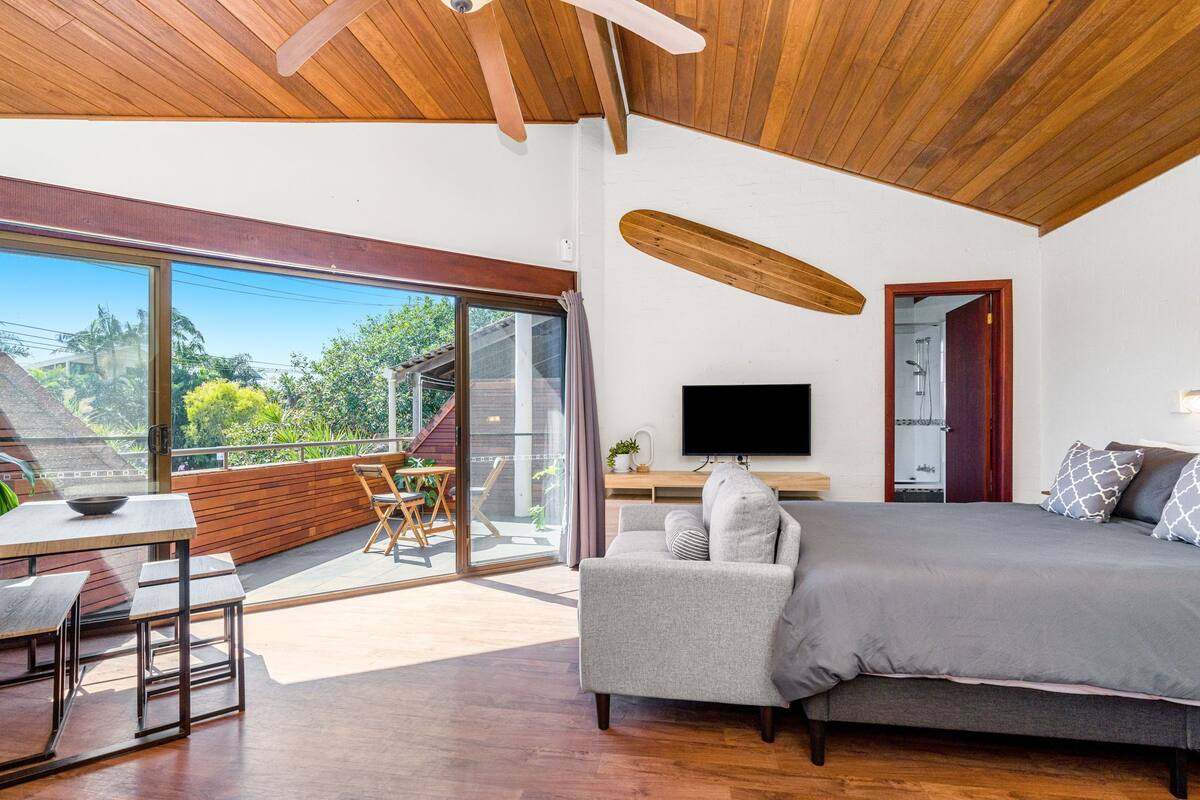 A modern bedroom with a large bed, a flat-screen TV, and a balcony with a dining area.