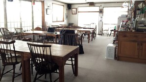 Un comedor con mesas y sillas de madera, una zona de cocina con electrodomésticos y ventanas amplias que dejan entrar luz natural.