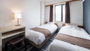 Hotellihuone, jossa on kaksi sänkyä, työpöytä, tuoli ja ikkuna, jossa on verhot.