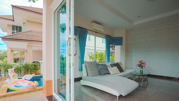 Una sala de estar moderna con una puerta de vidrio que da a una zona de piscina, un sofá con cojines y una mesita con un jarrón de flores.