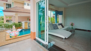 Habitación de hotel moderna con puerta de cristal que da a un balcón, una piscina y un área de descanso con sofá y mesa.