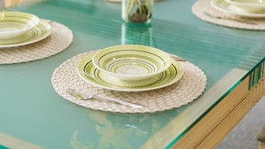 Una mesa de comedor con cubierta de vidrio, rodeada de sillas, y un jarrón con flores amarillas en el centro.