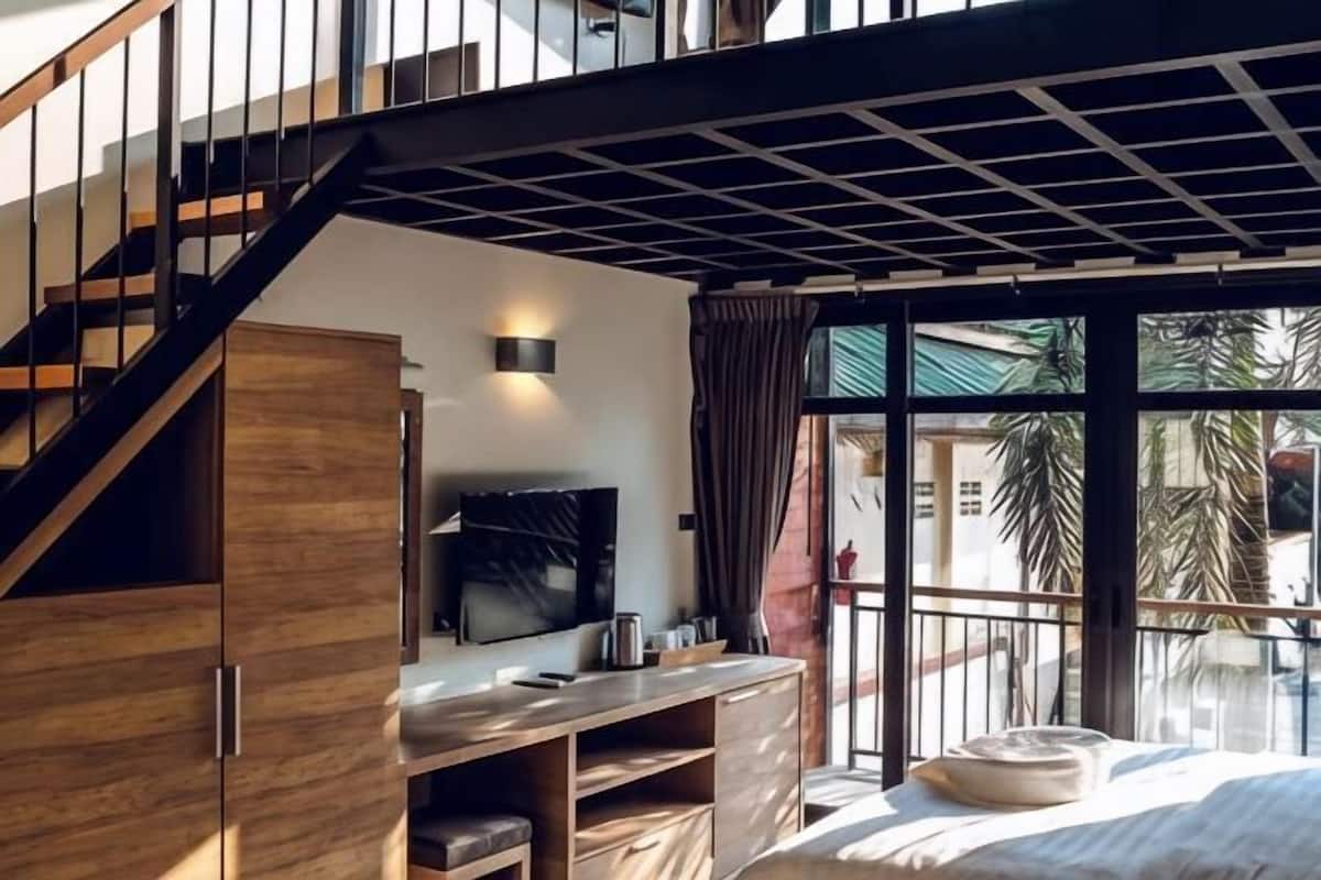 A modern room with a staircase, a flat-screen TV, a wooden cabinet, and a large window with a view of palm trees.