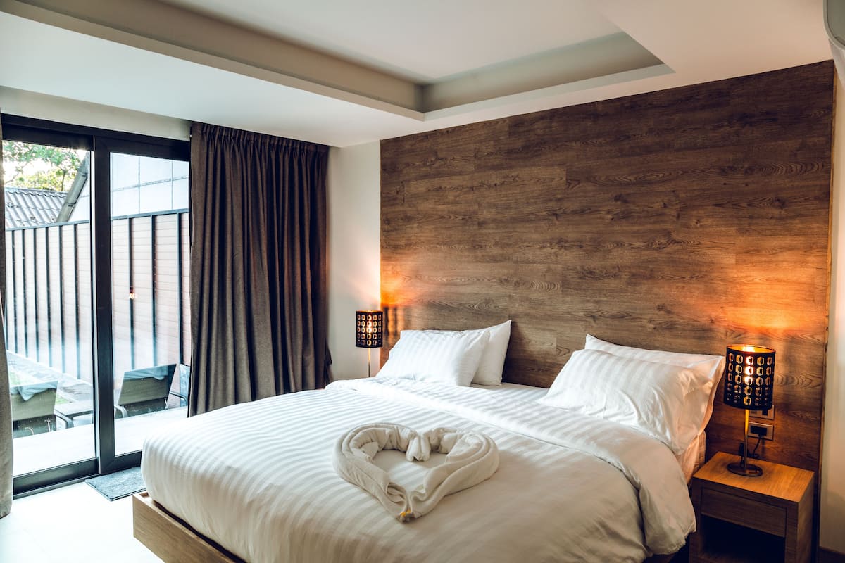 A hotel room with a large bed, two bedside lamps, a wooden headboard, and a view through a sliding glass door.
