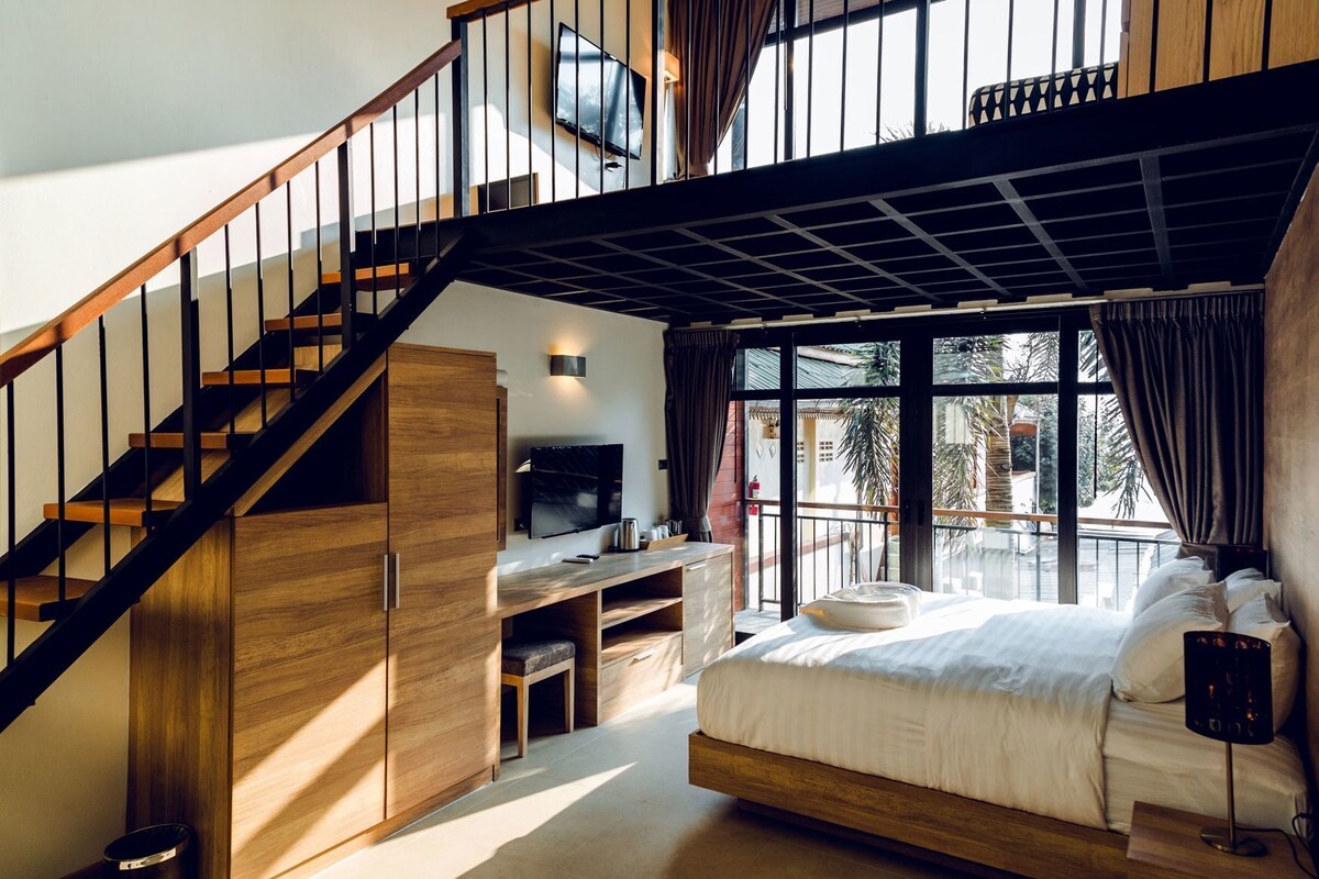 A bedroom with a bed, a desk, a TV, and a staircase.