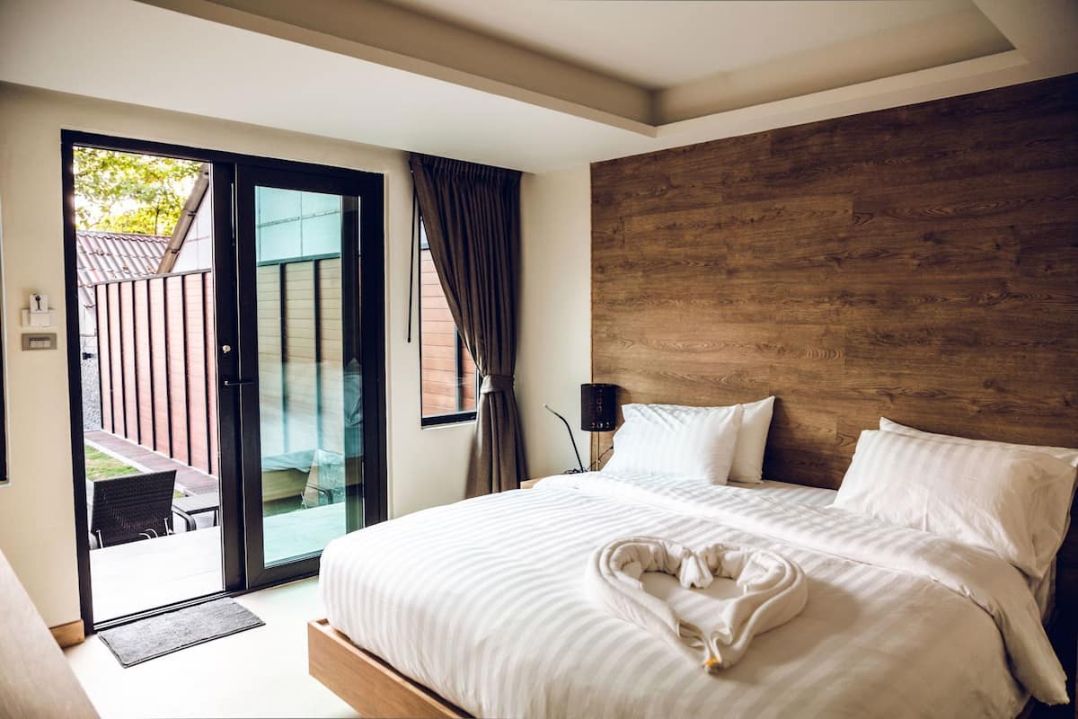 A bedroom with a large bed, a wooden headboard, a glass door leading to a balcony, and a small table with chairs.