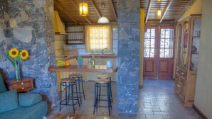 Un interior rústico con paredes de piedra, techo de madera, zona de bar con taburetes y una mesa de comedor.
