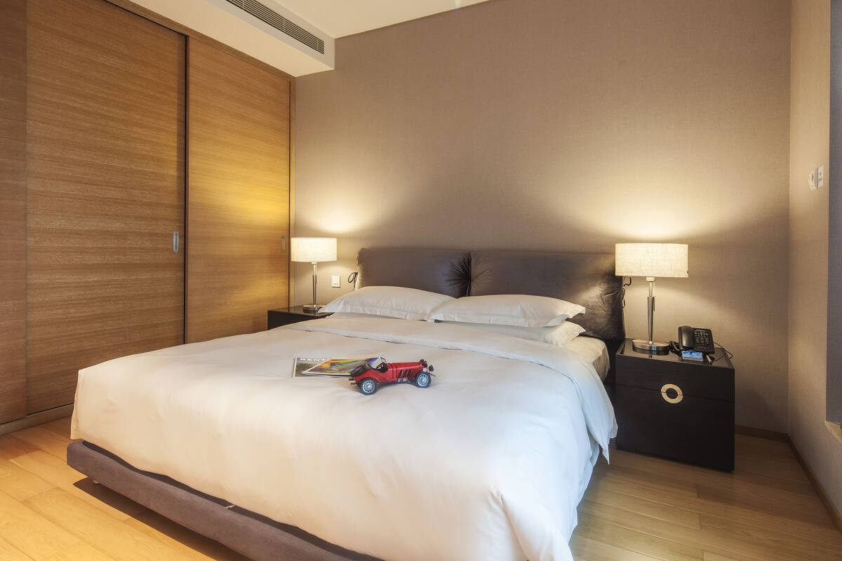 Une chambre d’hôtel moderne avec un grand lit, deux tables de chevet avec des lampes, une armoire en bois et une voiture jouet posée sur le lit.