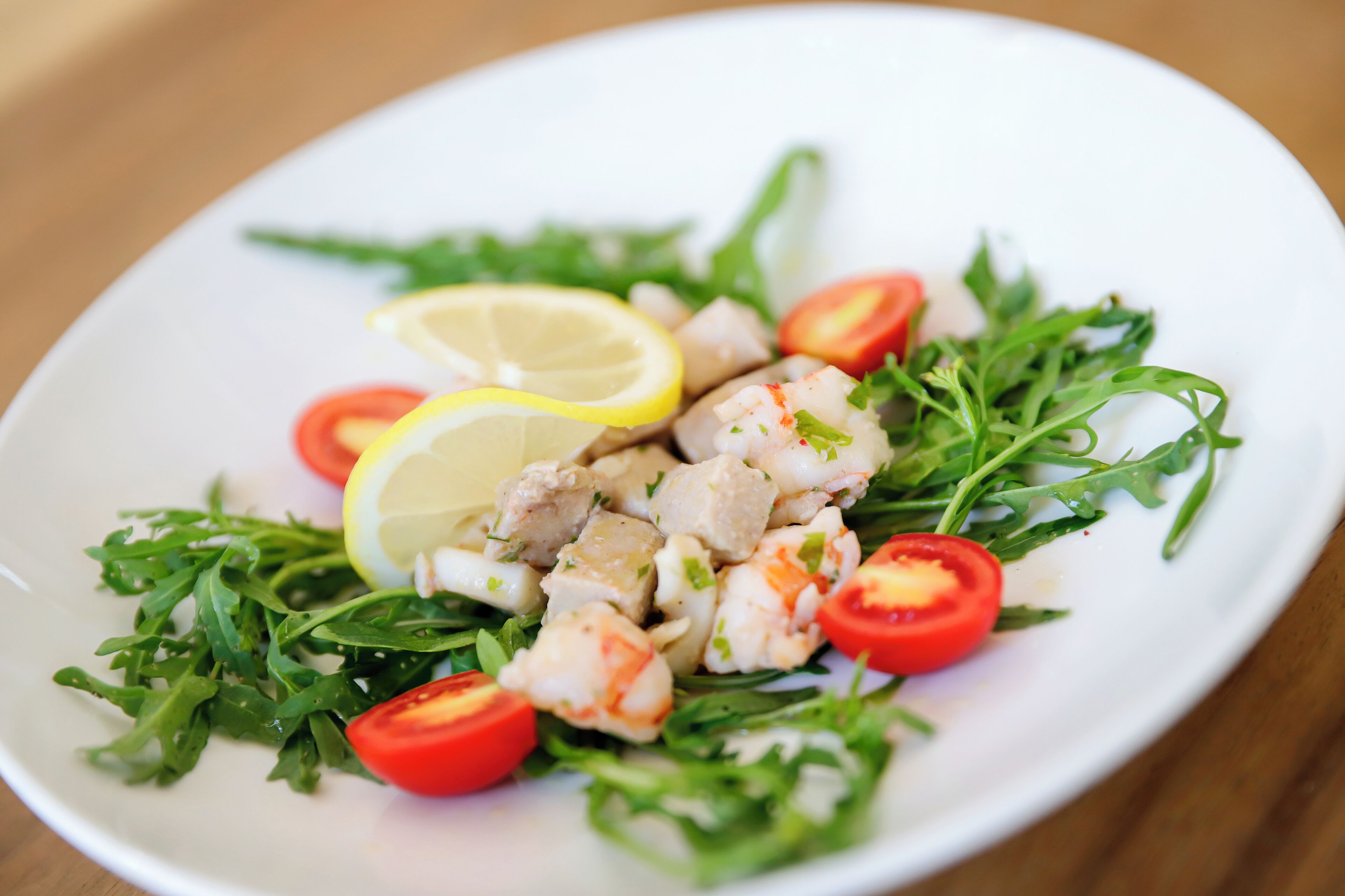 A plate of seafood salad with arugula and lemon slices.