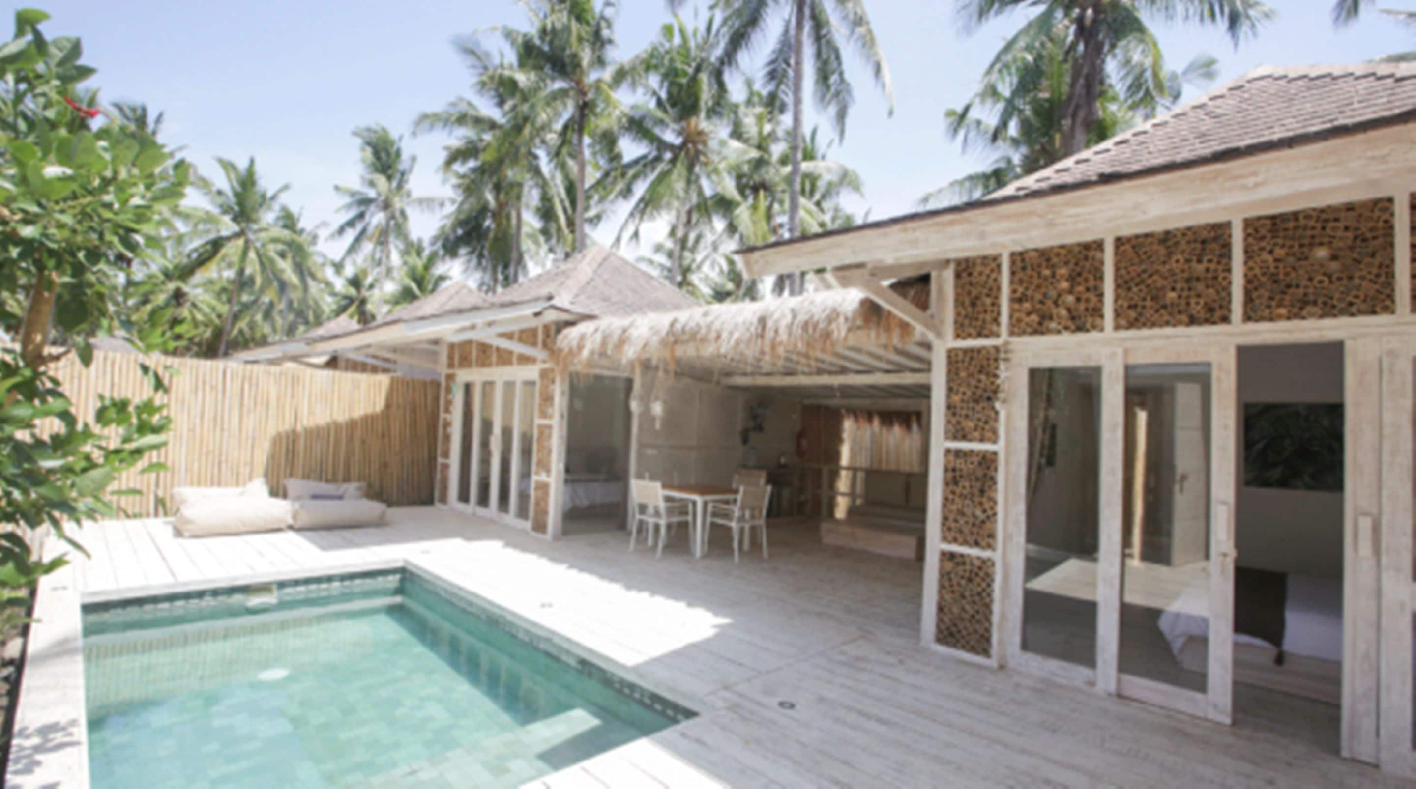 A poolside area with a pool, wooden deck, and a thatched-roof structure.