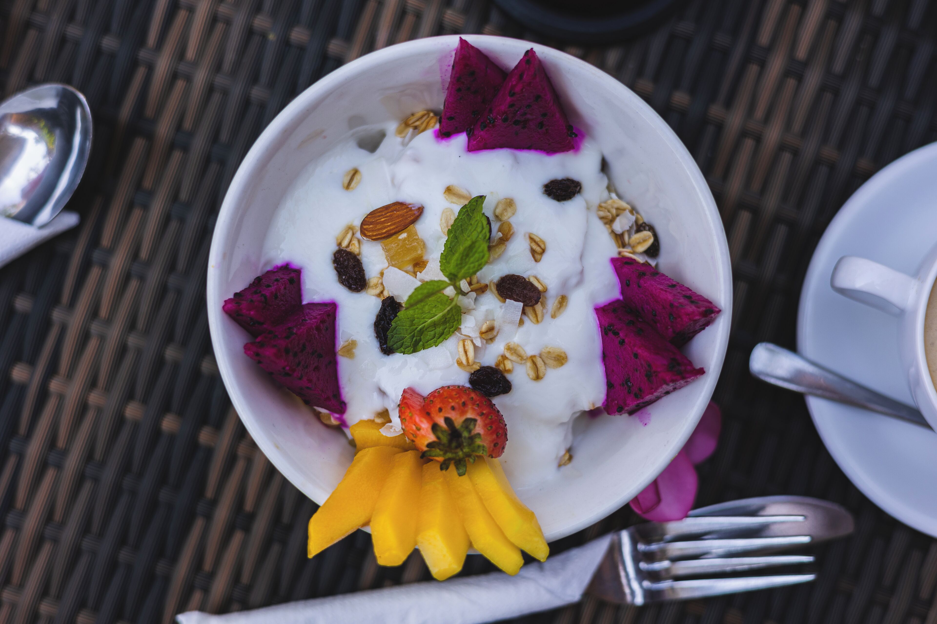 Un tazón de yogur cubierto con pitahaya, almendras y tajadas de mango.