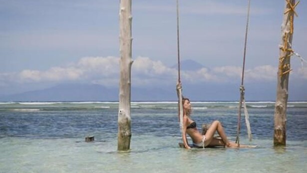A person sitting on a swing in shallow water with clear skies and distant mountains. - Villas Edenia (Gili Trawangan)