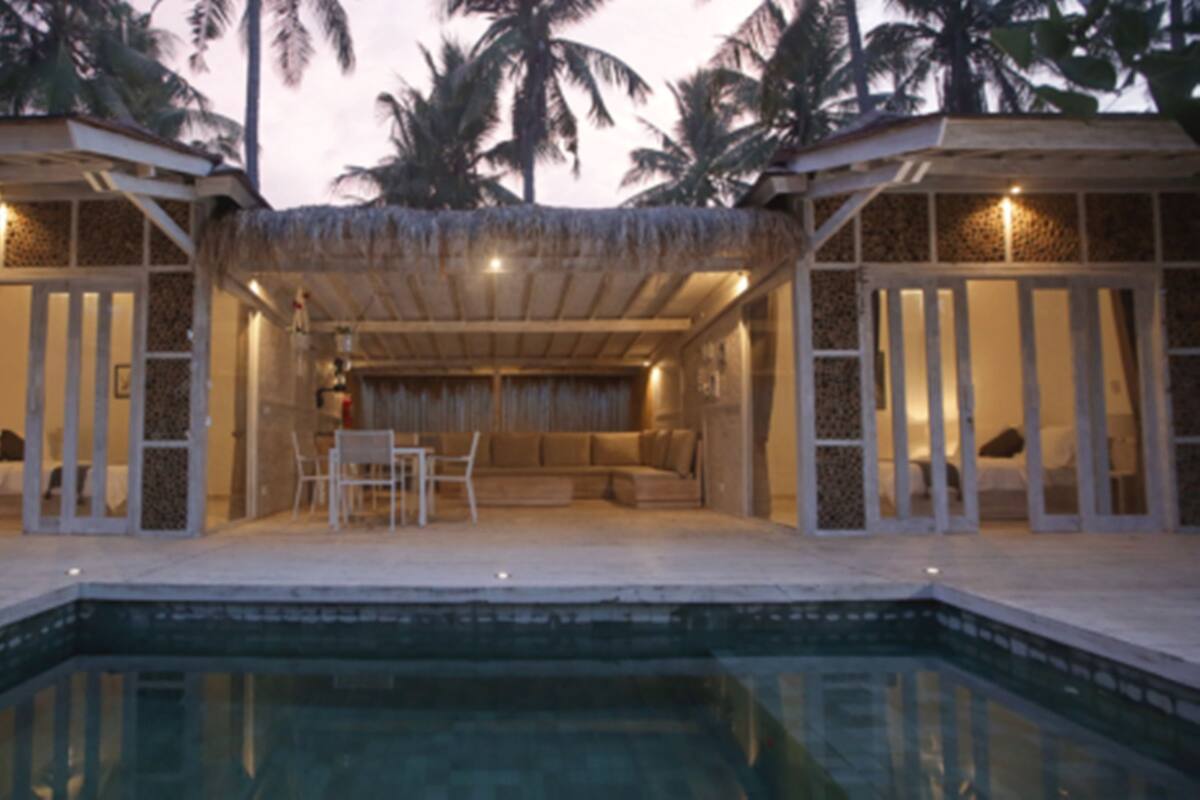 A poolside area with a covered seating area, palm trees, and a pool.