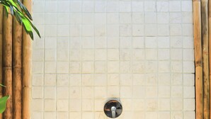 A tiled shower enclosure with a drain in the center, surrounded by bamboo and green plants. - Villas Edenia (Gili Trawangan)