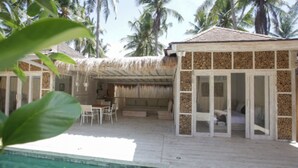A beachside resort with a thatched-roof structure, a pool, and palm trees in the background. - Villas Edenia (Gili Trawangan)