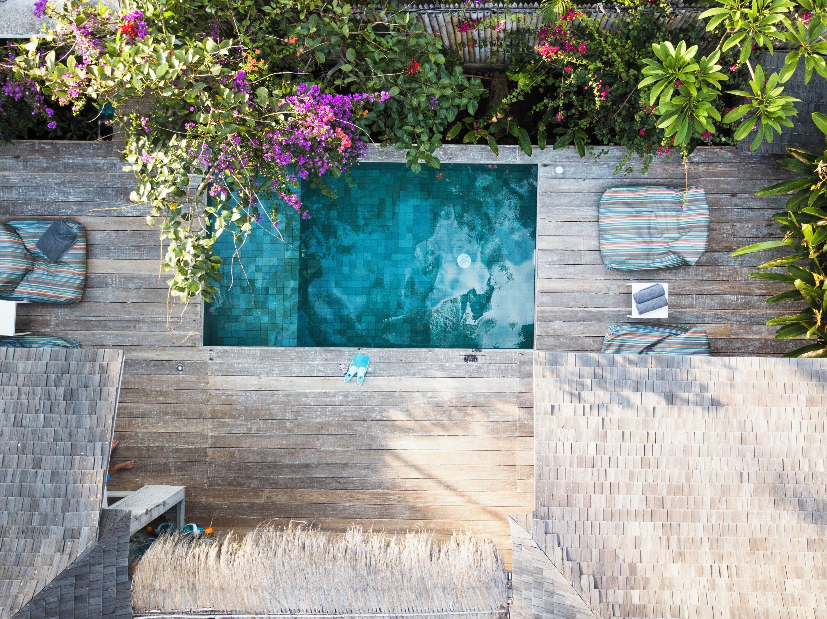 A swimming pool with a wooden deck, surrounded by lounge chairs and cushions.