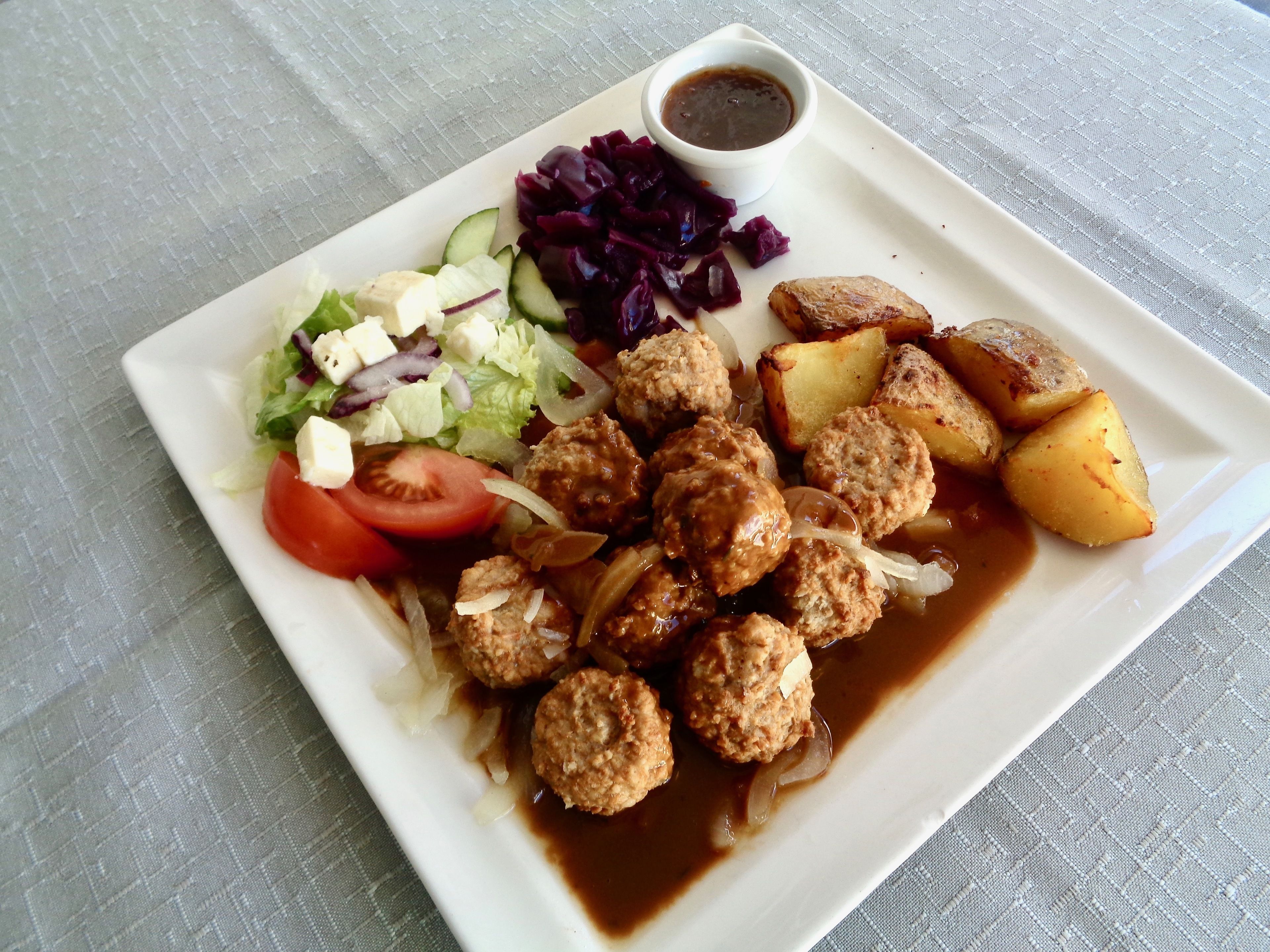 A plate of food with meatballs, potatoes, salad, and a side of red cabbage.