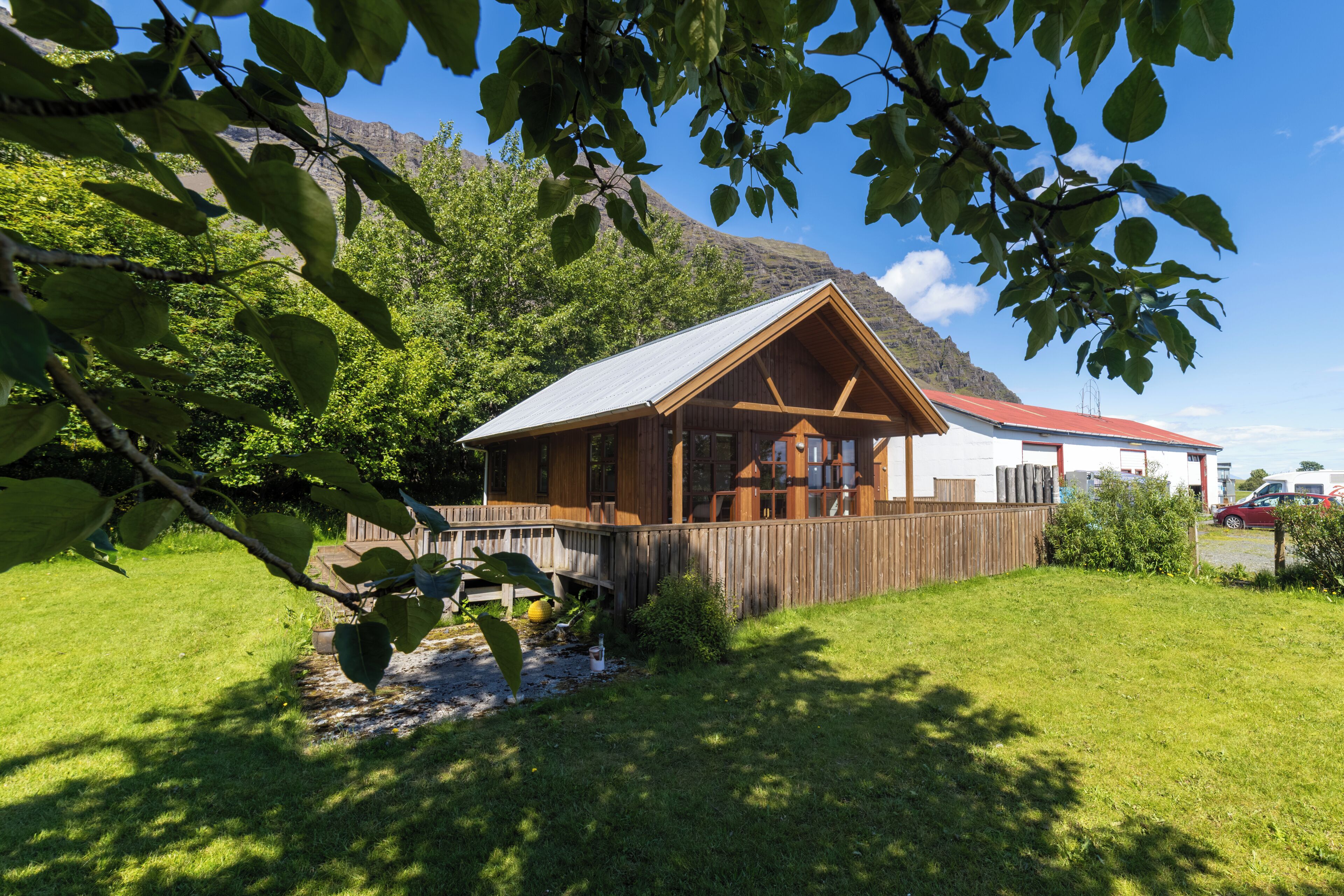 A wooden cabin with a sloped roof, surrounded by a wooden deck and a fenced yard.