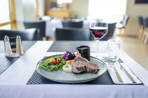 Una mesa de comedor con un plato de comida, una copa de vino tinto y saleros y pimenteros.