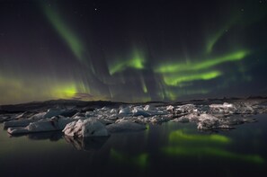 Vista noturna da aurora boreal sobre uma paisagem congelada com icebergs.