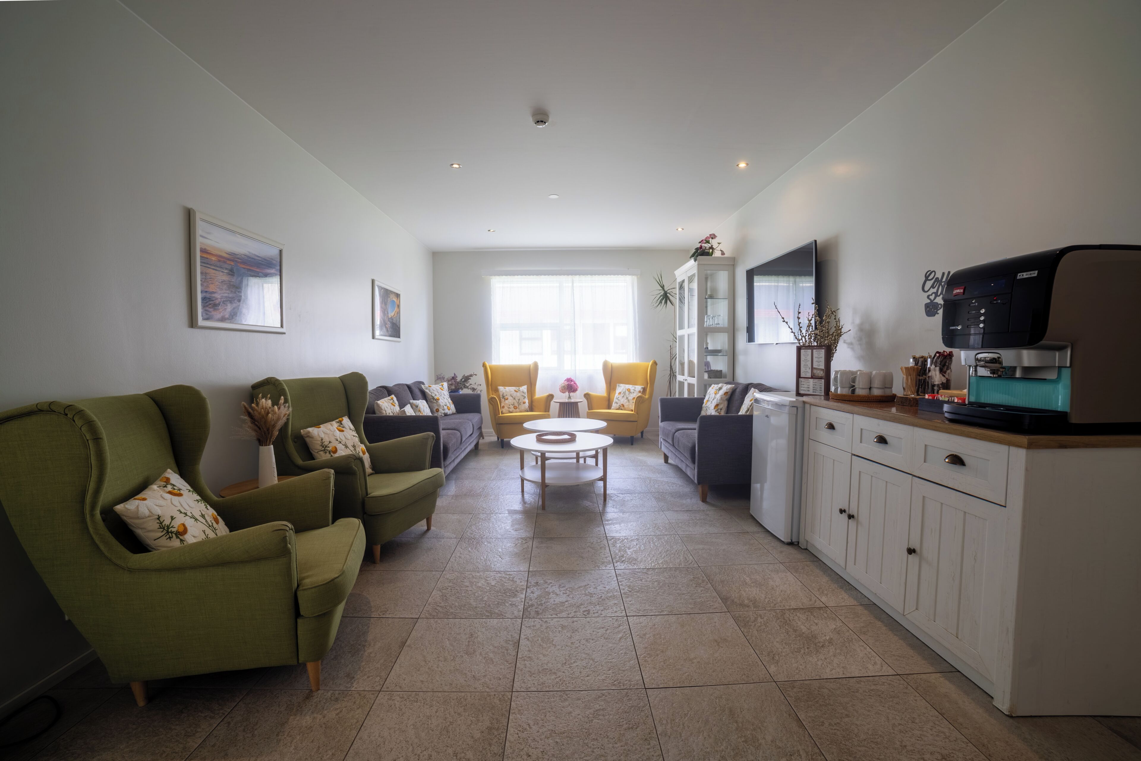 A modern living room with a sofa, armchairs, a coffee table, and a kitchen area with a coffee machine.