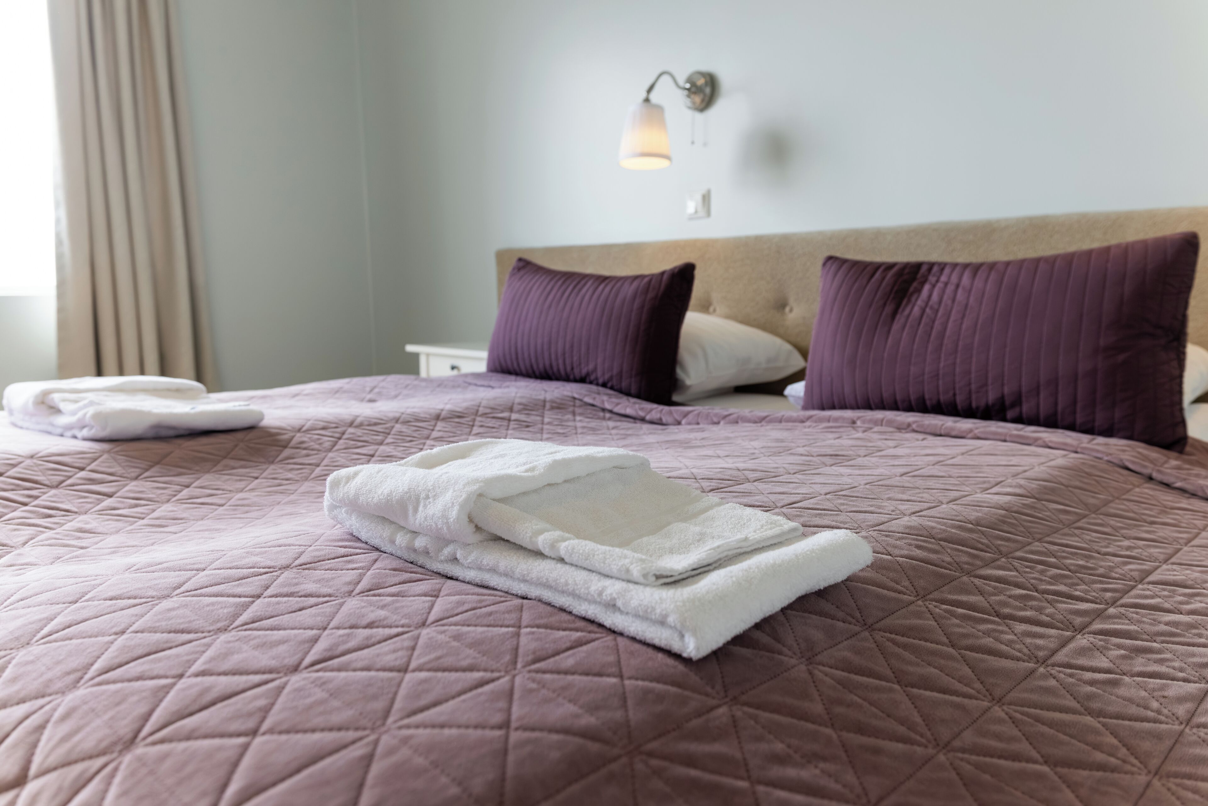Una cama bien hecha con un cubrecolchón acolchado, dos almohadas y una toalla blanca doblada.