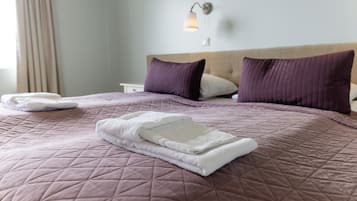 Una cama bien hecha con un cubrecolchón acolchado, dos almohadas y una toalla blanca doblada.