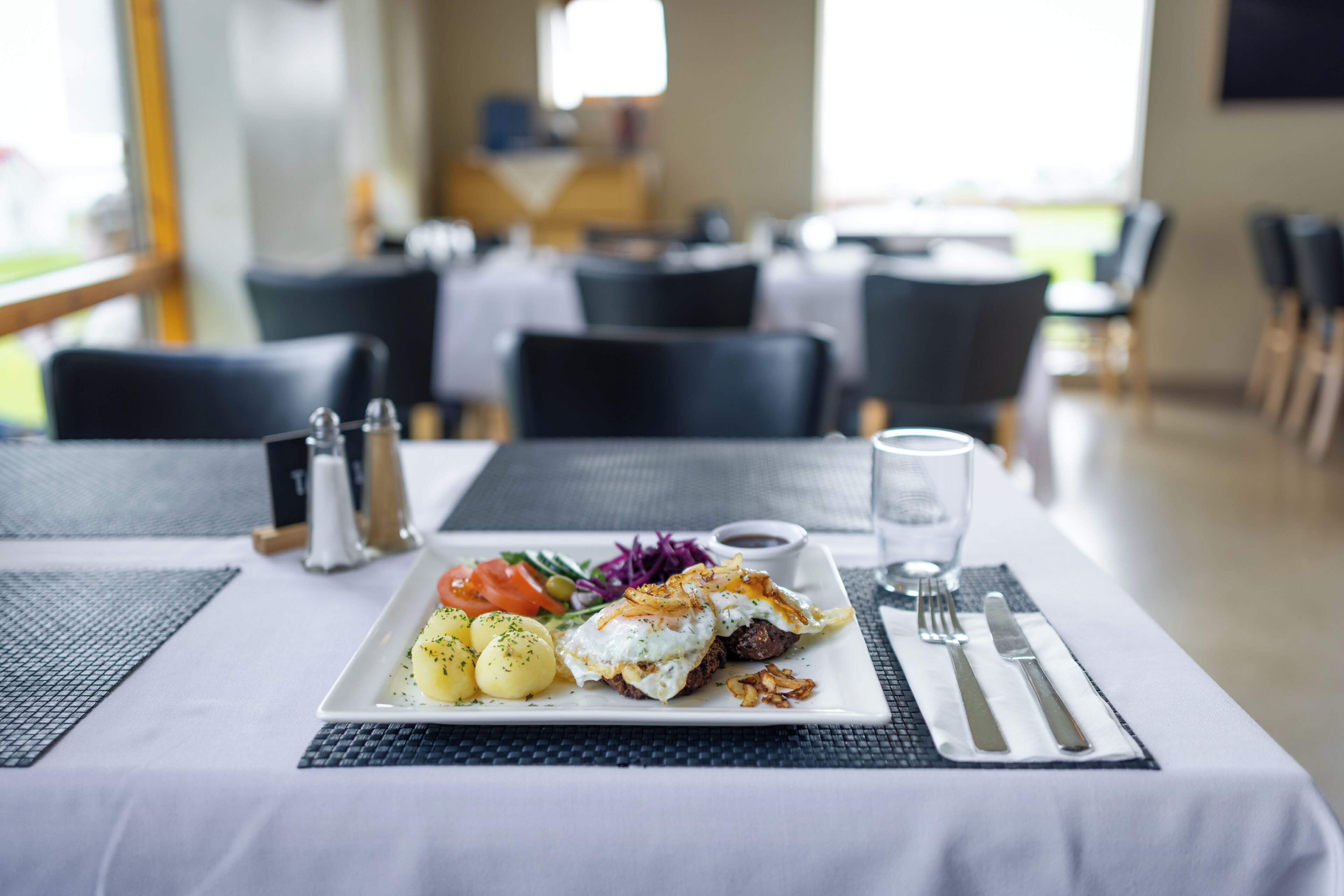 A dining table with a plate of food, cutlery, and a glass of water.