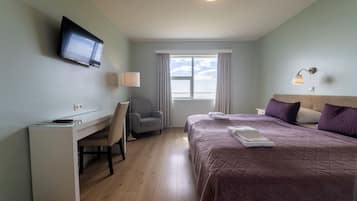 A hotel room with a bed, a desk, a chair, a television, and a window with curtains.