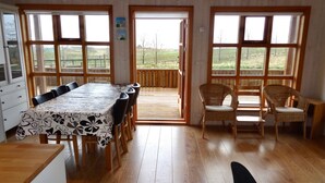 A dining area with a long table and chairs, large windows, and a view of the outdoors.