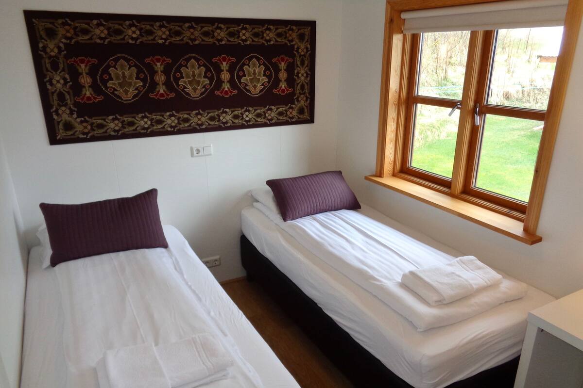 Ein Zimmer mit zwei Einzelbetten, einem Fenster mit Blick auf Grünflächen und einem Wandteppich als Dekoration.