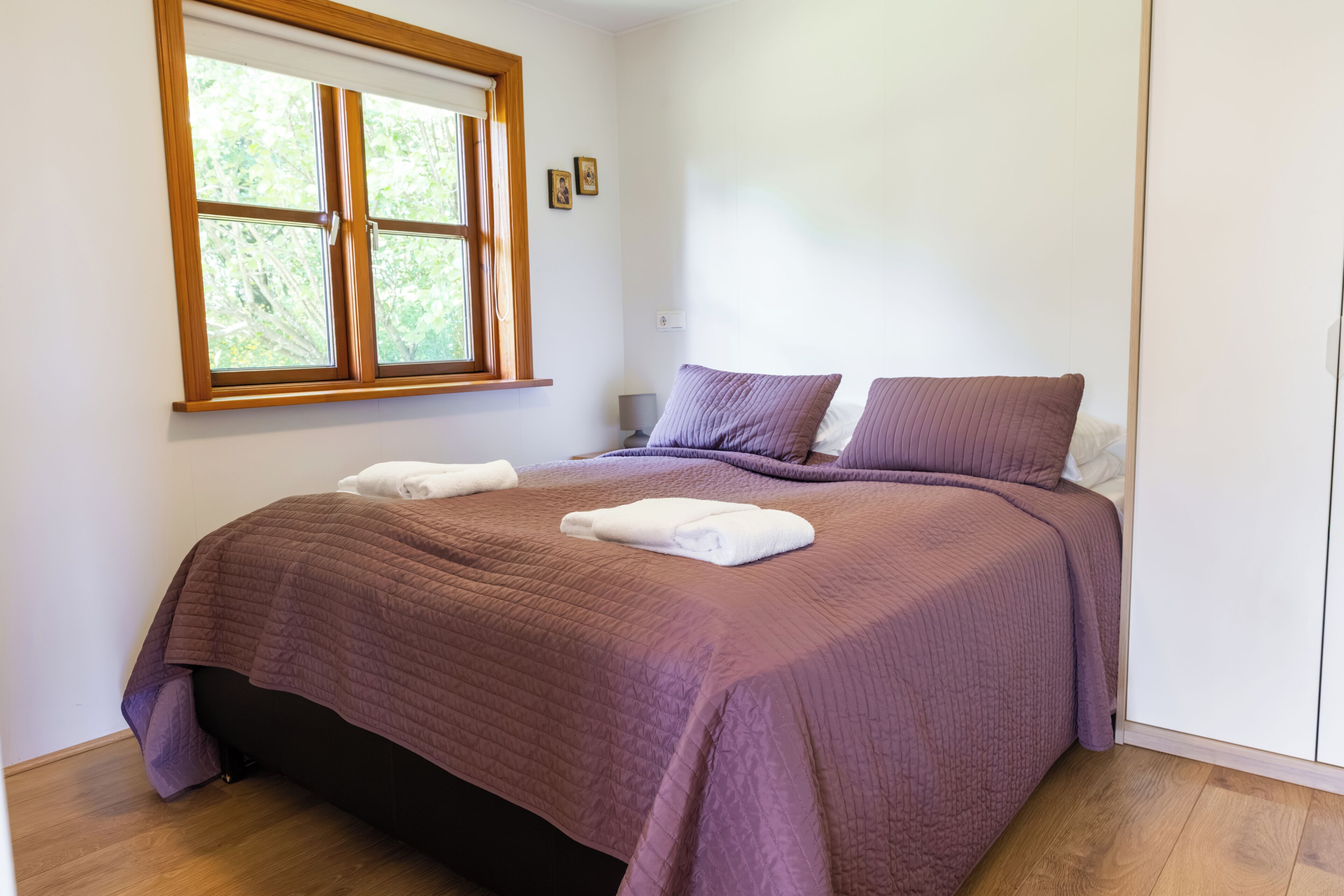 Un dormitorio con cama, almohadas, una ventana y una mesita de noche.