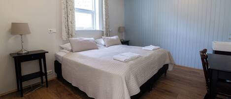 A bedroom with a bed, two bedside tables, a window with curtains, a desk, and a chair.